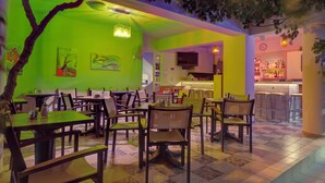 A restaurant with multiple tables and chairs, a bar area, and a television screen. - Costas & Chrysoula (Agios Vasileios)