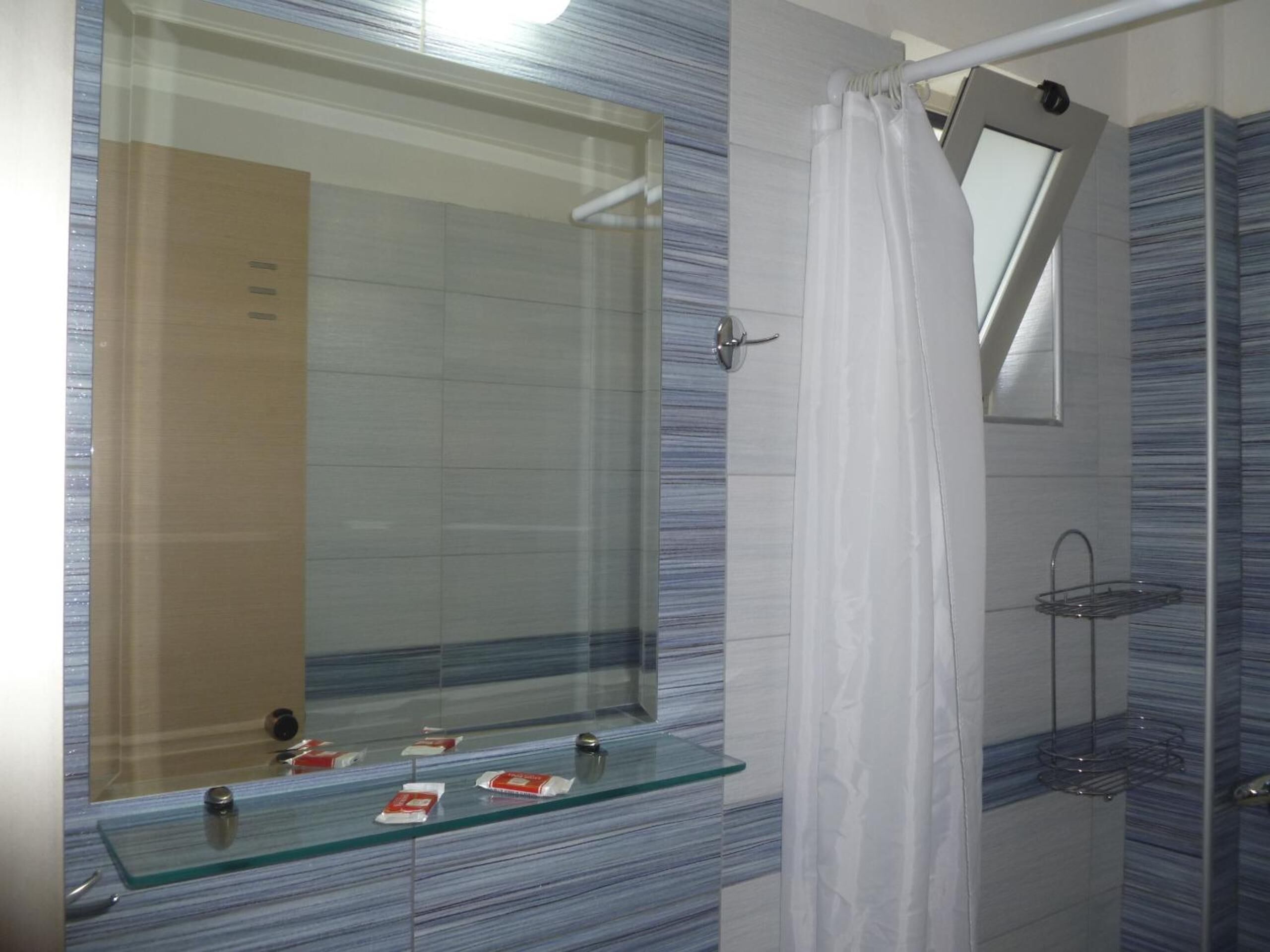A bathroom with a glass shelf, a shower, and a mirror.