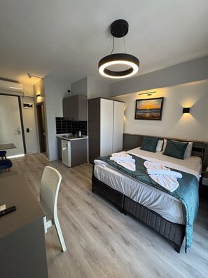 Una habitación de hotel moderna con cama, escritorio, kitchenette y un cuadro en la pared.