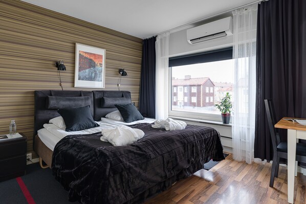 A modern hotel room with a large bed, a desk, and a window with a city view.