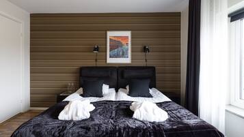 Una habitación de hotel moderna con una cama grande, cabecera con líneas horizontales, dos lámparas de noche y un cuadro enmarcado en la pared.