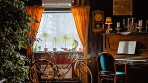 A room with a piano, a bicycle, and a window with curtains. - Wärdshuset C. Dickens (Fagersta)