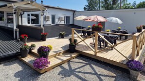 A covered outdoor seating area with tables and chairs, surrounded by potted plants and umbrellas. - Wärdshuset C. Dickens (Fagersta)