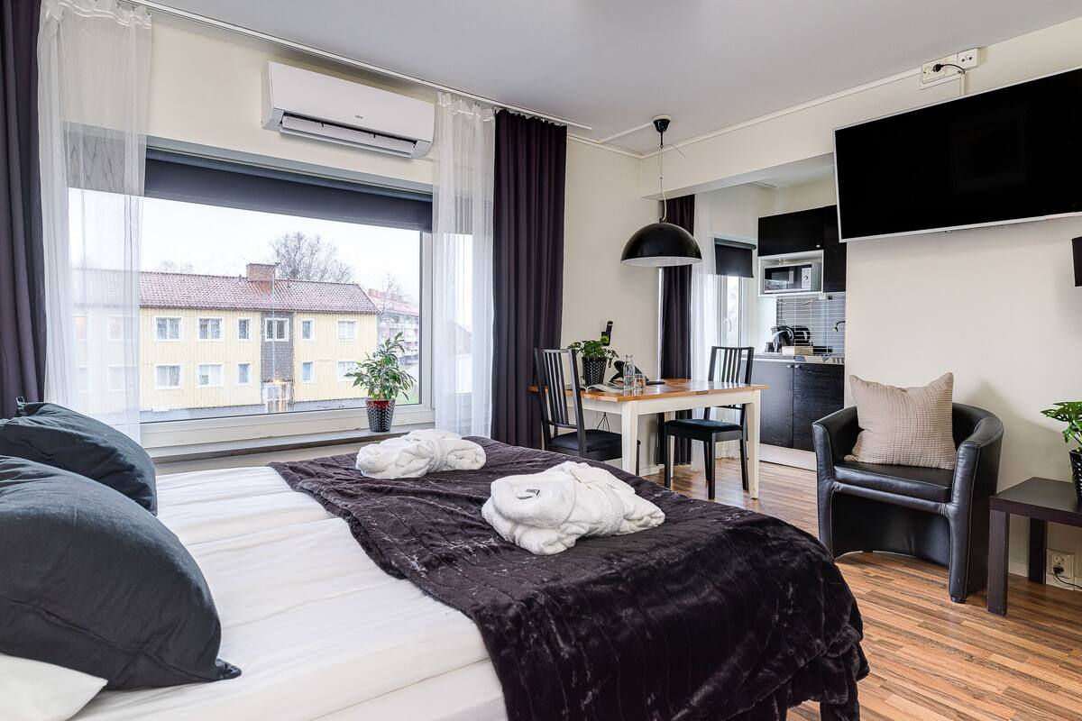 A modern hotel room with a large bed, a dining area, and a kitchen.