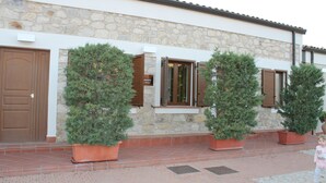 Un edificio con paredes de piedra, puertas de madera y ventanas con contraventanas. Hay plantas en macetas frente a las ventanas.