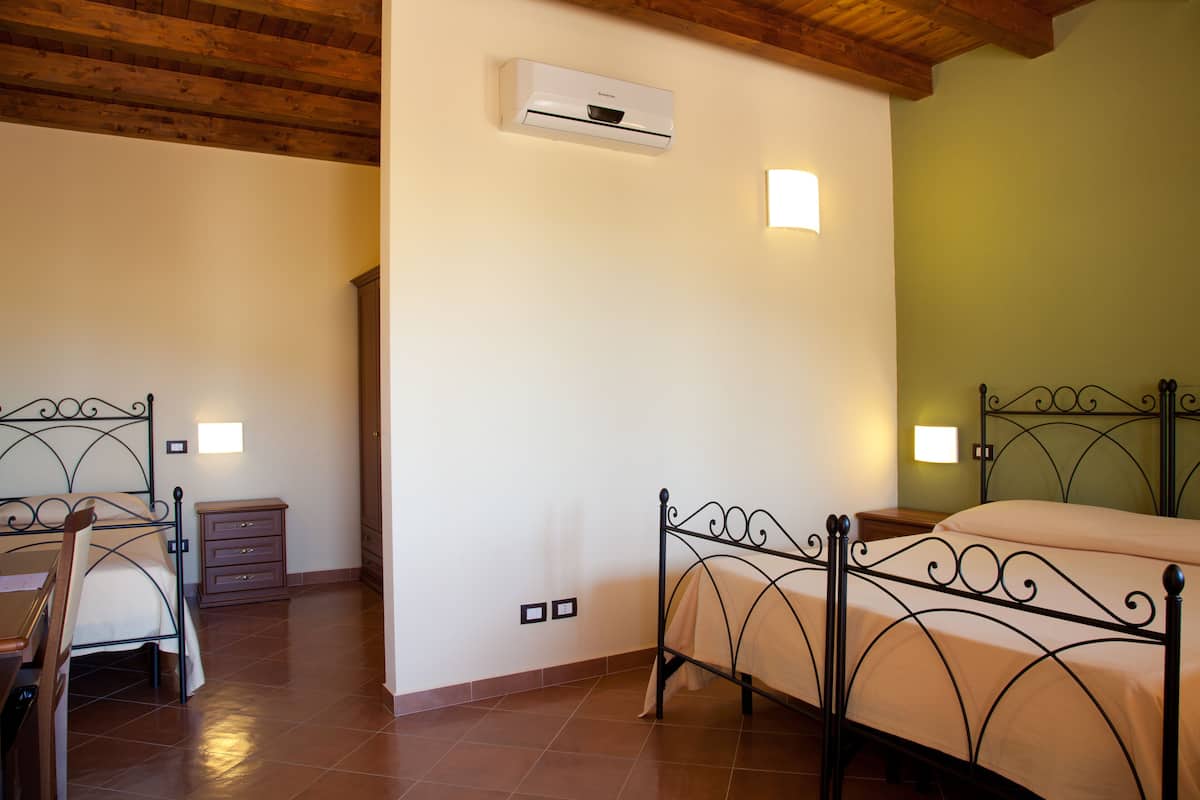 Un dormitorio con cama, mesitas de noche, una silla y un equipo de aire acondicionado en la pared.