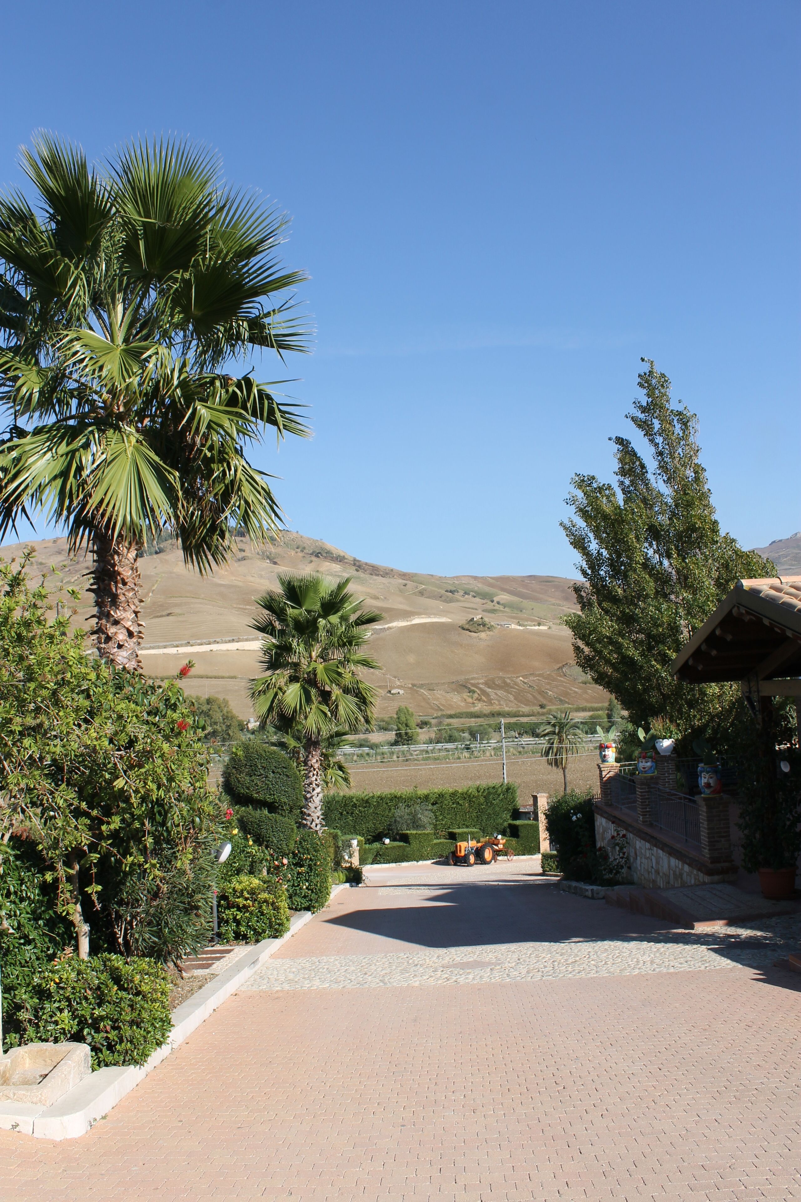 A paved pathway leading to a building with a view of a hilly landscape.