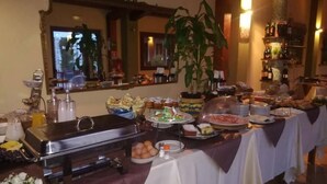 Mesa de buffet con diversos alimentos, un encargado de buffet y una planta decorativa.
