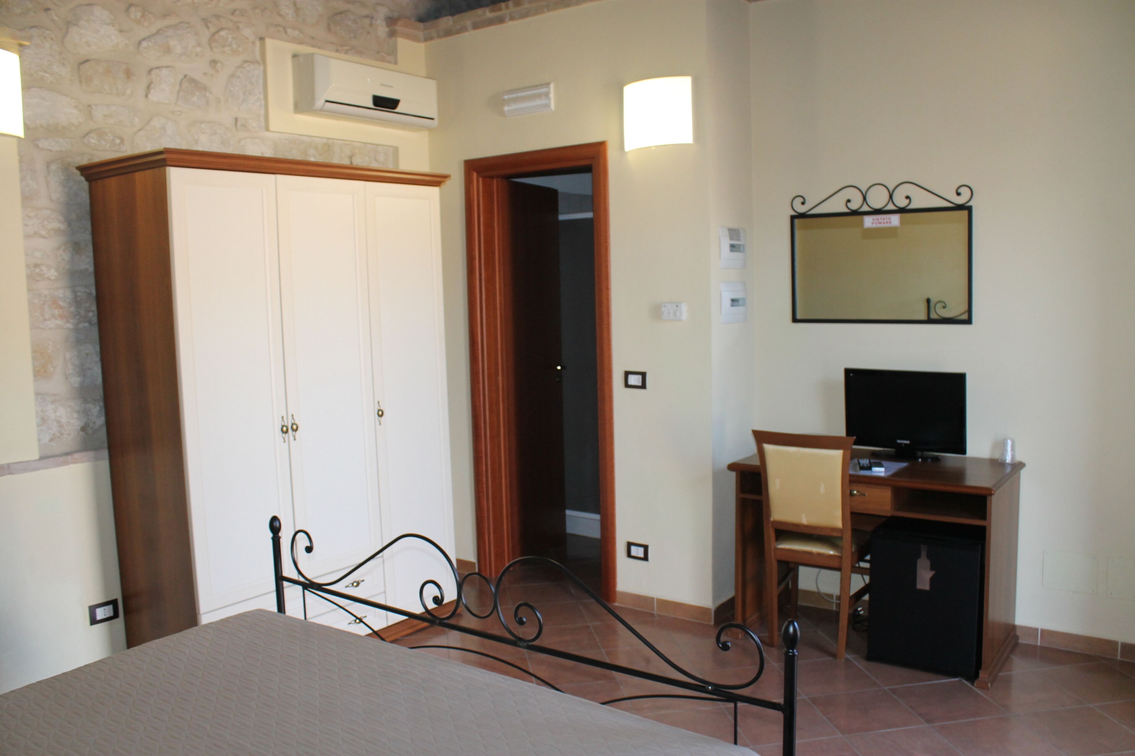 A bedroom with a bed, wardrobe, desk, chair, television, and a mirror on the wall.