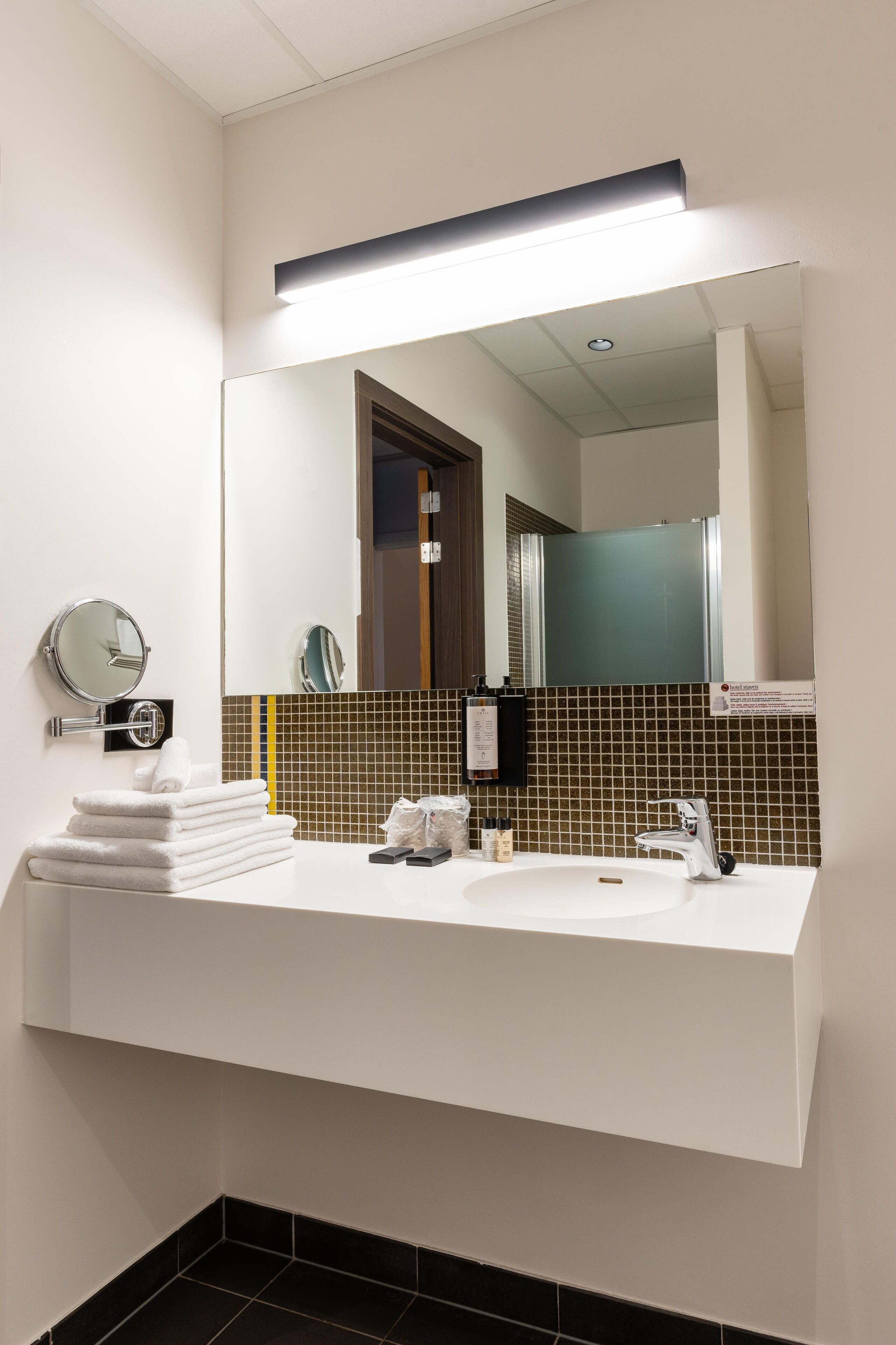 A modern bathroom with a white sink, a large mirror, and a towel stack.