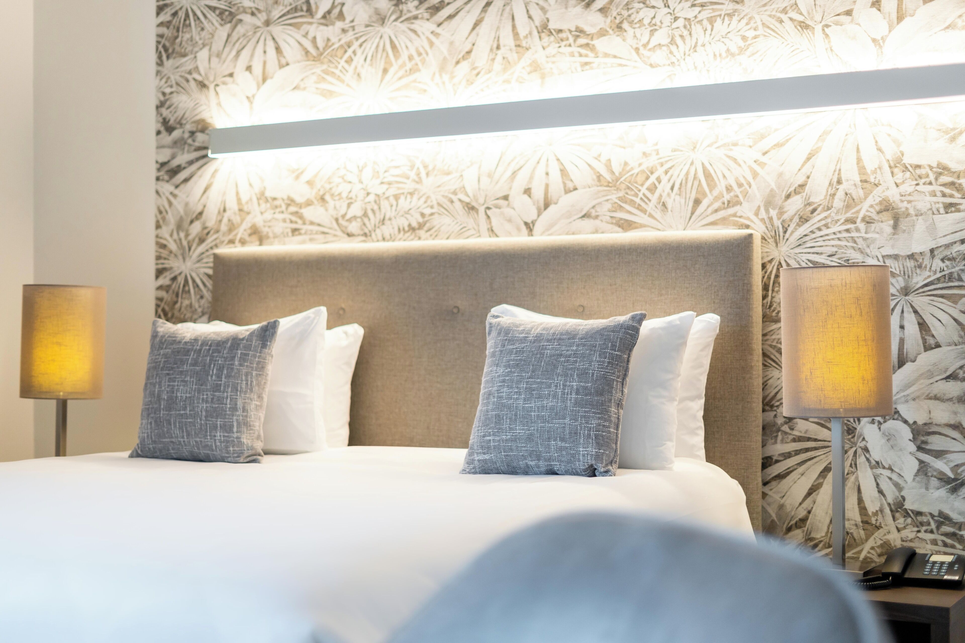 A hotel room with a large bed, two bedside lamps, and a floral wallpaper.