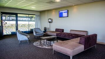 A modern waiting area with a sofa, armchairs, a coffee table, and a television screen.