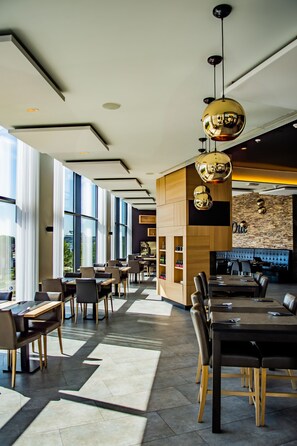 A modern hotel lobby with large windows, a central wooden reception desk, and multiple dining areas with tables and chairs. - Hotel Stayen (Sint-Truiden)