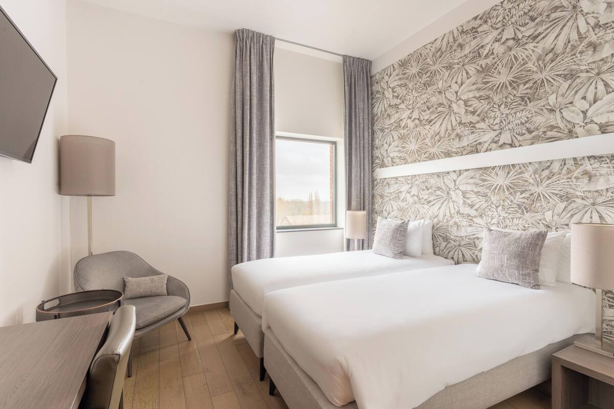 A hotel room with a bed, a desk, a chair, a TV, and a window with curtains.