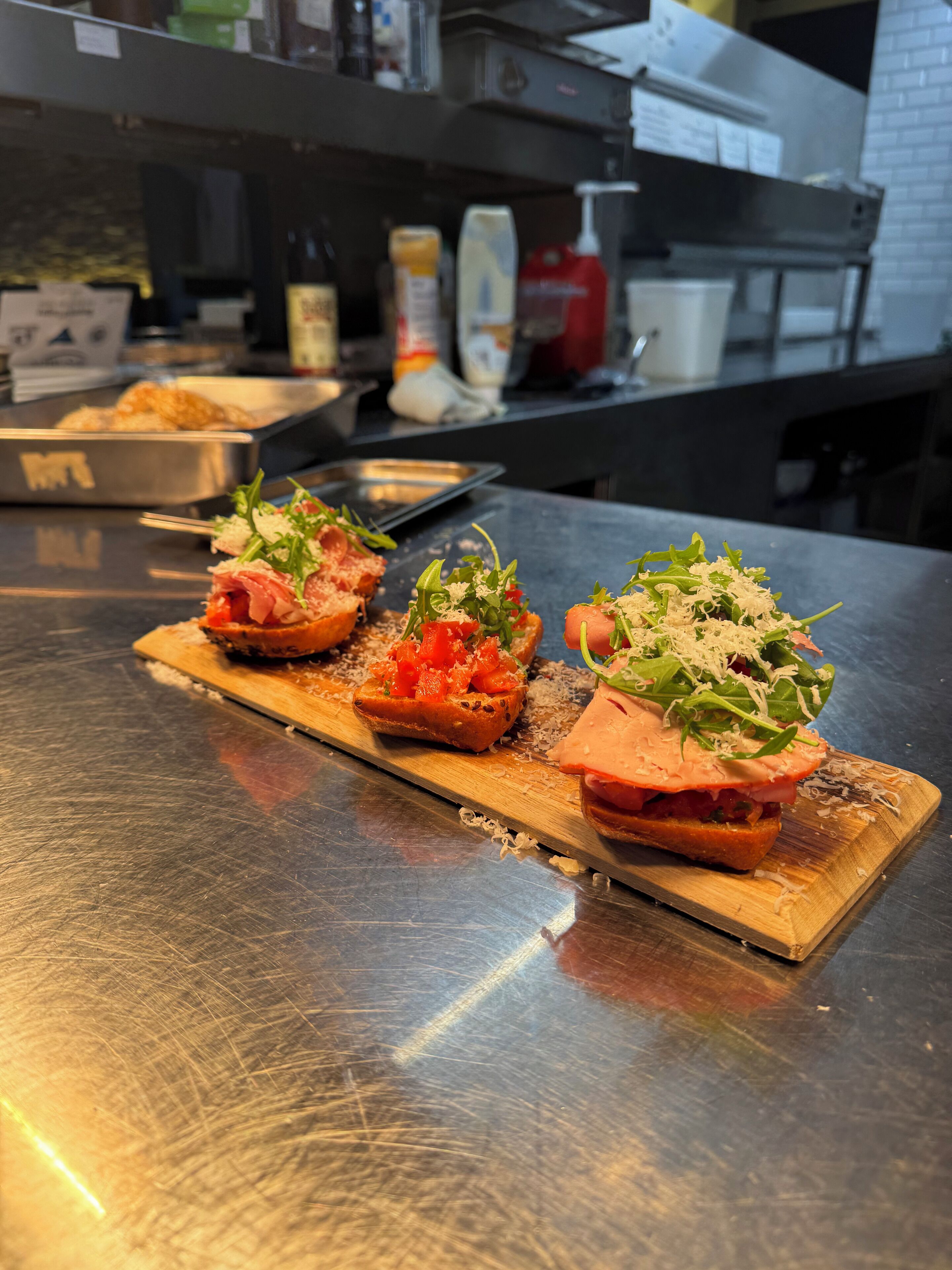 Un tagliere di legno con tre panini aperti su un ripiano in acciaio inox.