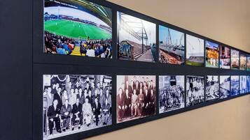 Un mur où sont exposées une série de photographies historiques, notamment des images d’un stade, de bâtiments industriels et de rassemblements officiels.