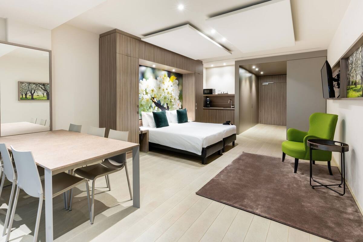Une chambre à coucher moderne avec un lit, une table de chevet et un fauteuil vert.
