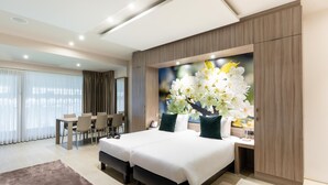 A modern hotel room with a large bed, a dining area, and a wall-mounted artwork of flowers.