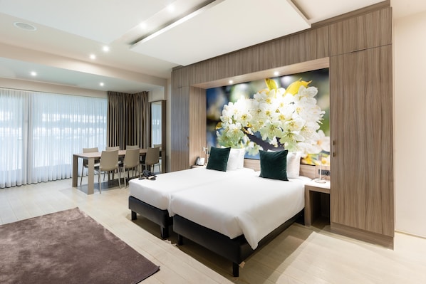 A modern hotel room with a large bed, a dining area, and a wall-mounted artwork of flowers. - Hotel Stayen (Sint-Truiden)