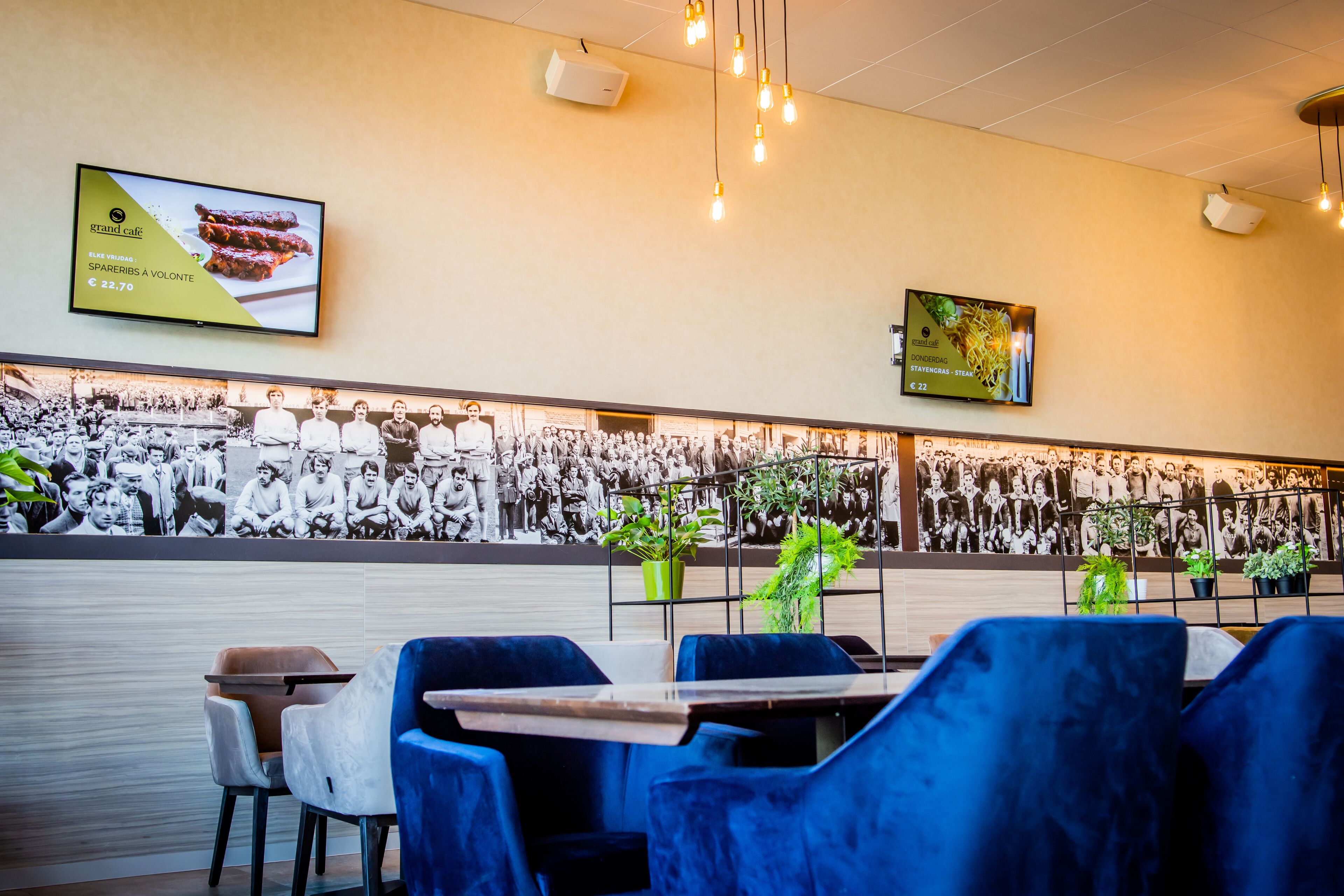 A restaurant with a long wall of black and white photos, blue velvet chairs, and a menu board.