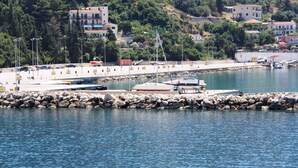 A marina with boats docked, a rocky breakwater, and buildings in the background. - Anastazia Hotel (Kefalonia)
