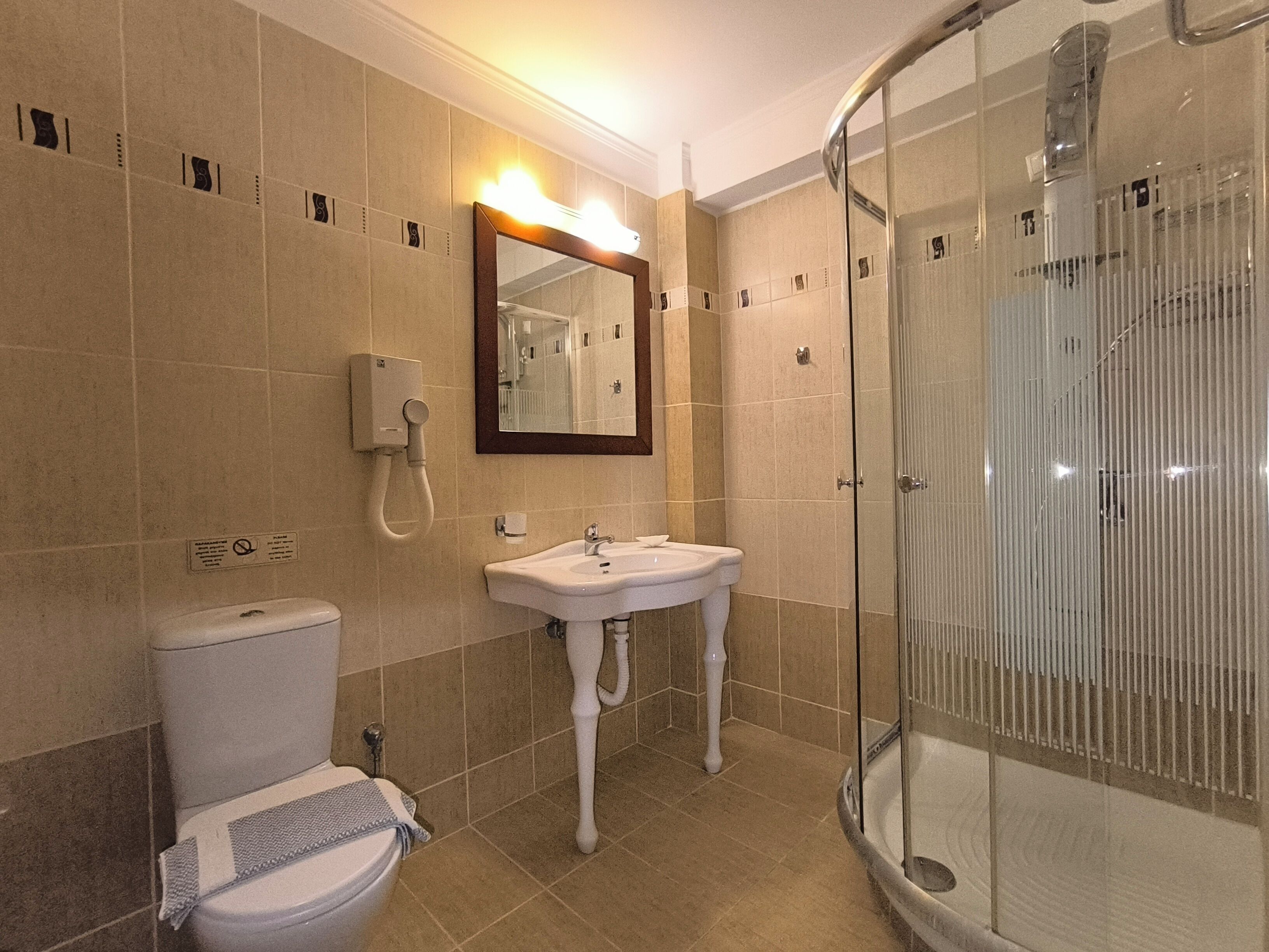Un baño con inodoro, lavabo, espejo y ducha con mampara de vidrio.