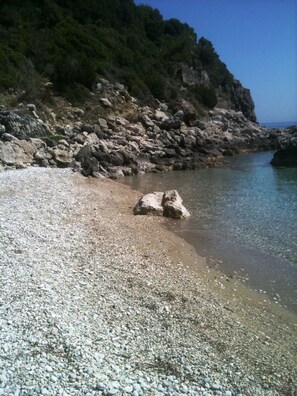 A pebble beach with clear water and a rocky cliff in the background. - Anastazia Hotel (Kefalonia)