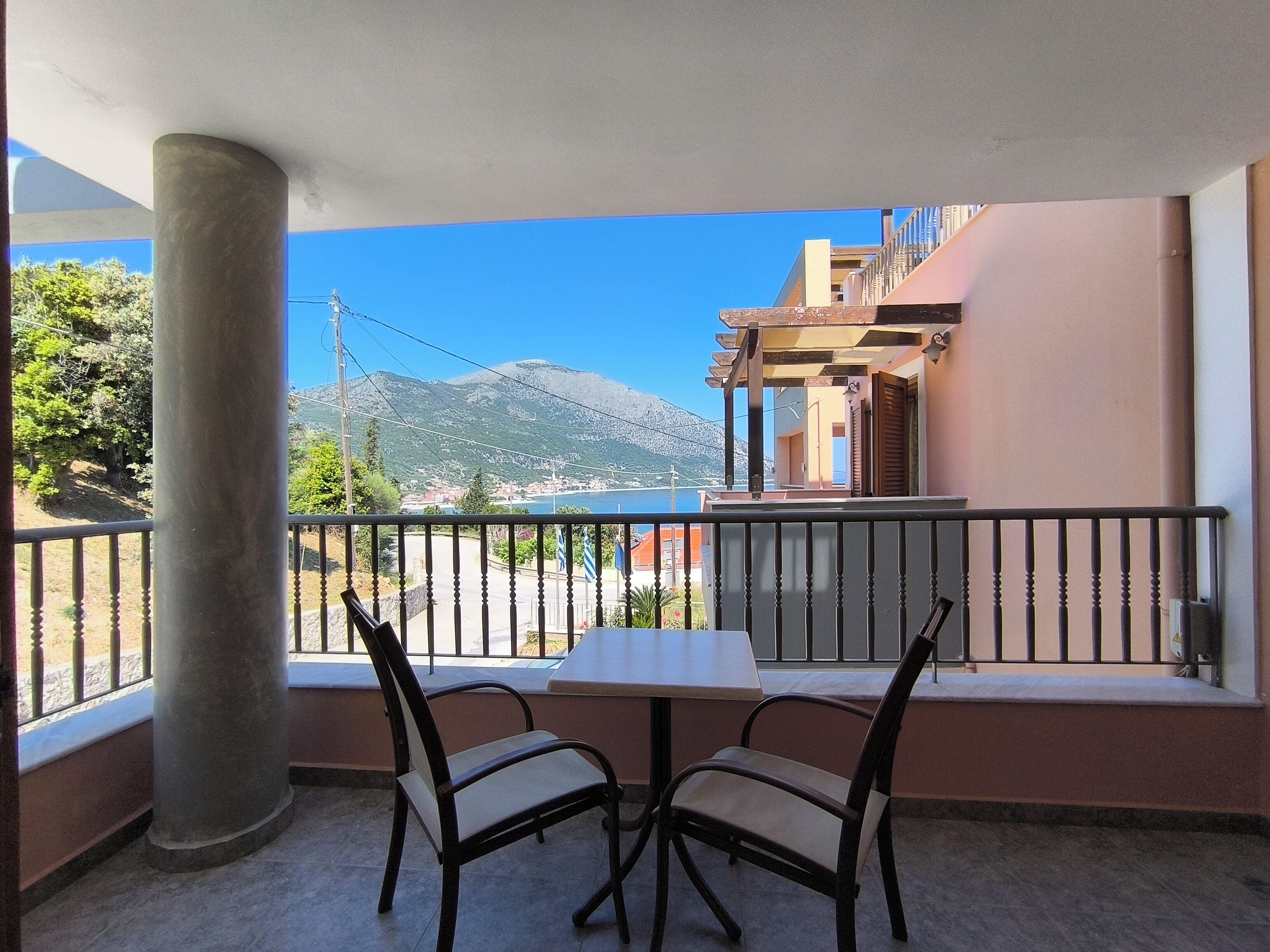 A balcony with two chairs and a table, overlooking a mountain and a body of water.