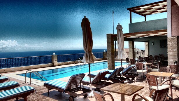 A rooftop pool area with lounge chairs, umbrellas, and a view of the ocean. - Anastazia Hotel (Kefalonia)