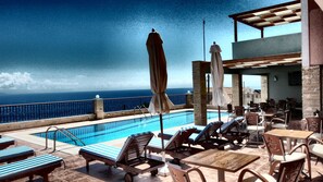A rooftop pool area with lounge chairs, umbrellas, and a view of the ocean. - Anastazia Hotel (Kefalonia)