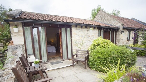 A stone building with a tiled roof, a wooden bench, and a small table. - Beeches Farmhouse Country Cottages & Rooms (Bradford-on-Avon)