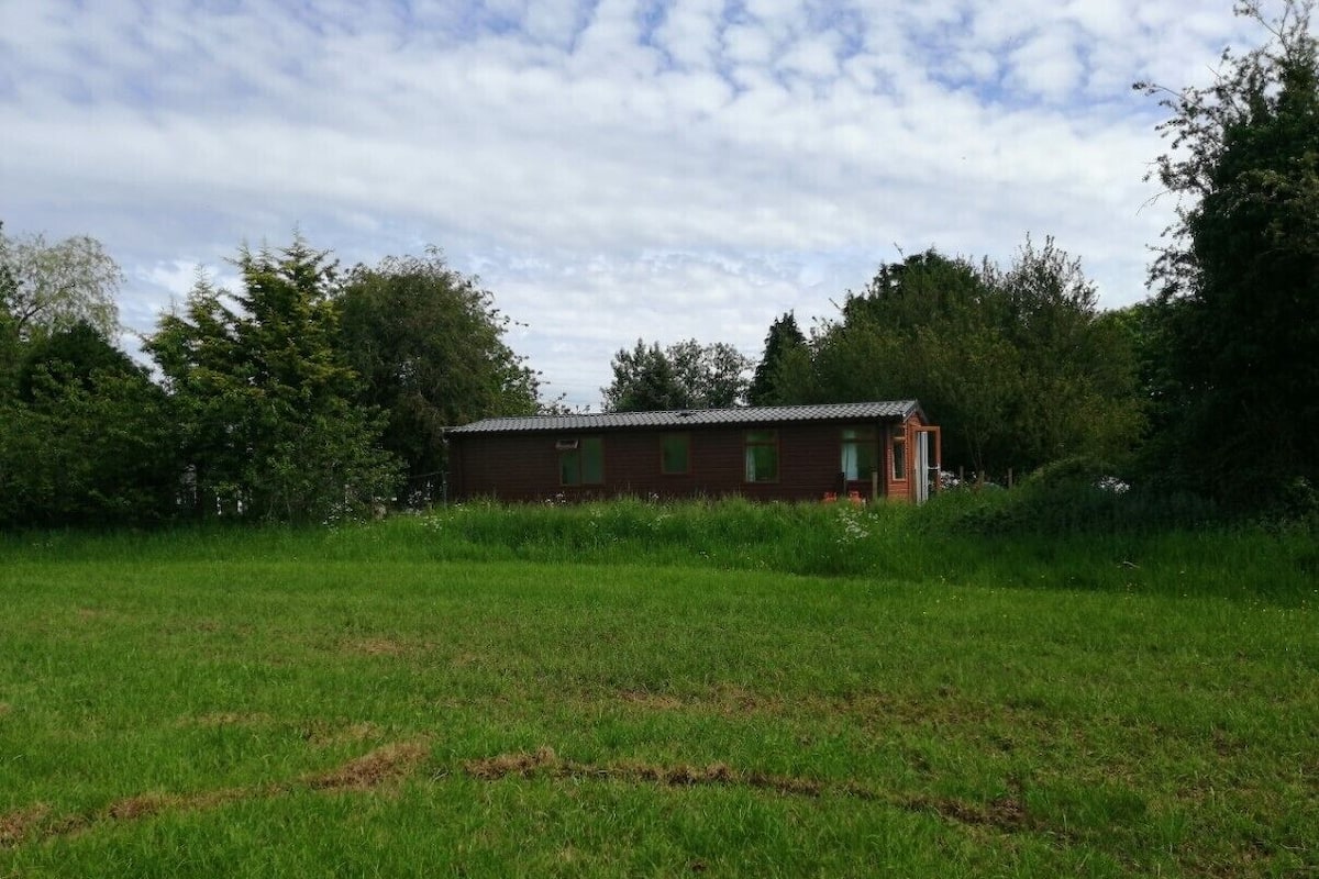 Un bâtiment en briques rouges, doté d’un toit plat, entouré d’un champ verdoyant et d’arbres.