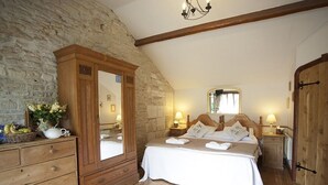 A bedroom with a stone wall, wooden furniture, a large bed with white linens, and a chandelier. - Beeches Farmhouse Country Cottages & Rooms (Bradford-on-Avon)