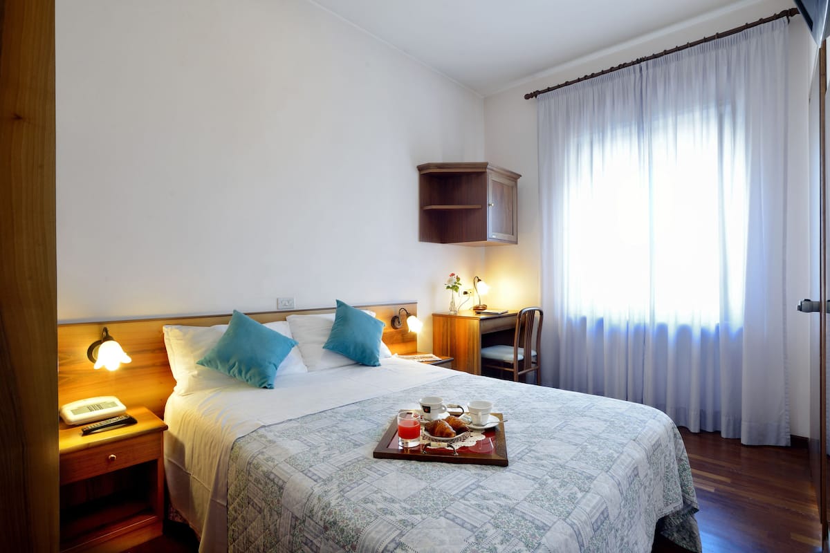A neatly made bed with a tray of breakfast, a bedside lamp, and a desk with a chair.