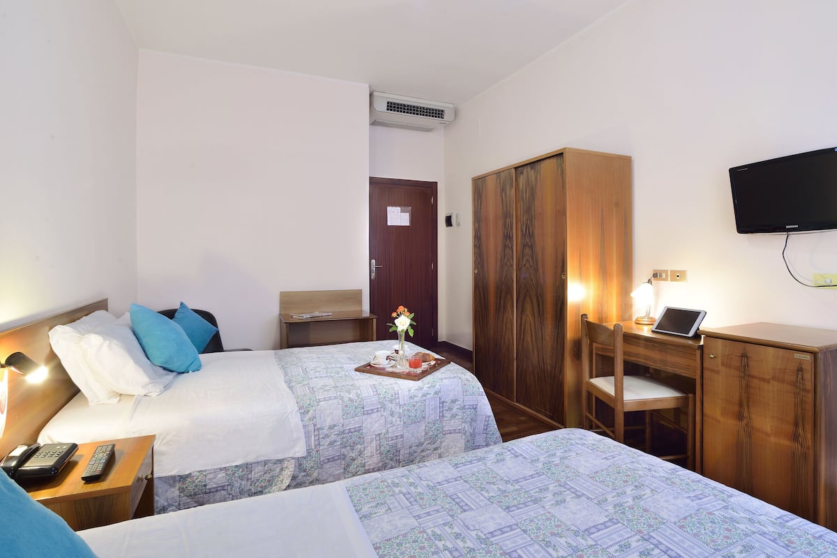 A hotel room with two beds, a desk with a computer, a TV, and a wardrobe.