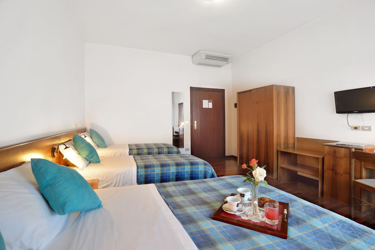 A hotel room with two beds, a wooden wardrobe, a television, and a tray with breakfast items.