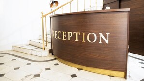 A reception desk with the word "RECEPTION" on it, a staircase with a golden railing, and a globe on a shelf. - Hotel Diplomat (Tbilisi)