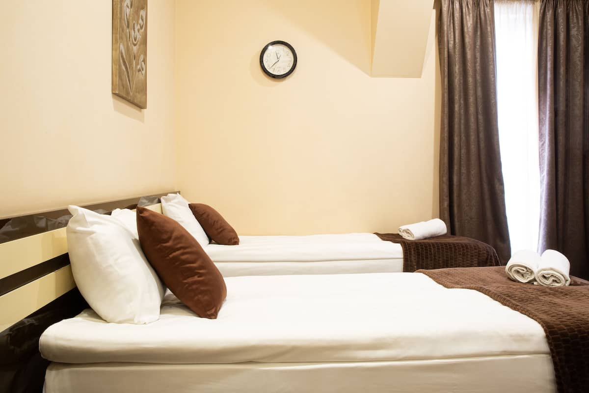 Ein Hotelzimmer mit zwei Betten, einer Wanduhr und einem Fenster mit Vorhängen.