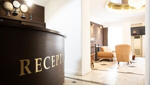 A reception area with a wooden reception desk, a chandelier, and a brick wall. - Hotel Diplomat (Tbilisi)