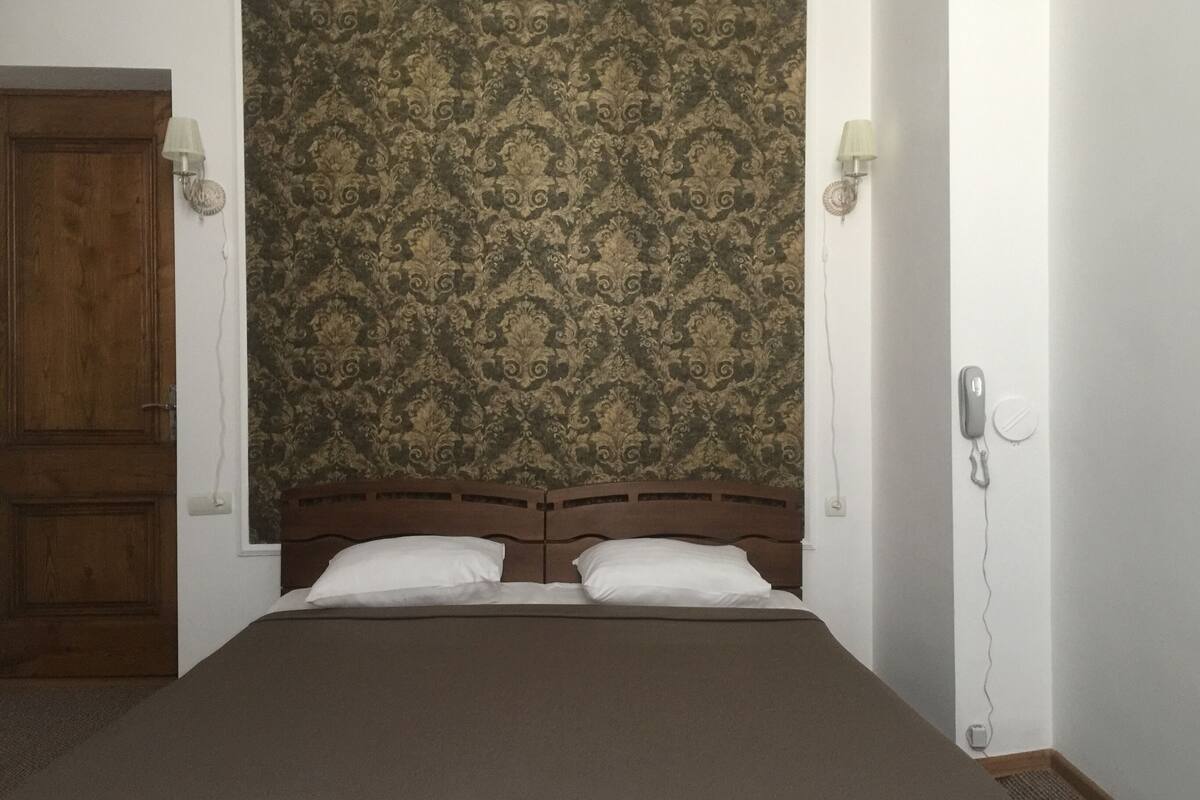 Ein Schlafzimmer mit einem hölzernen Kopfteil, zwei weißen Kissen, einer braunen Bettdecke und einer gemusterten Tapete.