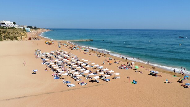A beach with rows of sunbeds and umbrellas, a clear sky, and calm sea. - ETHOS Bertolina Wellness Urban Living. (Albufeira)