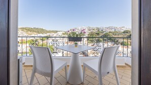 A balcony with two white wicker chairs and a table, overlooking a cityscape with buildings and greenery. - ETHOS Bertolina Wellness Urban Living. (Albufeira)