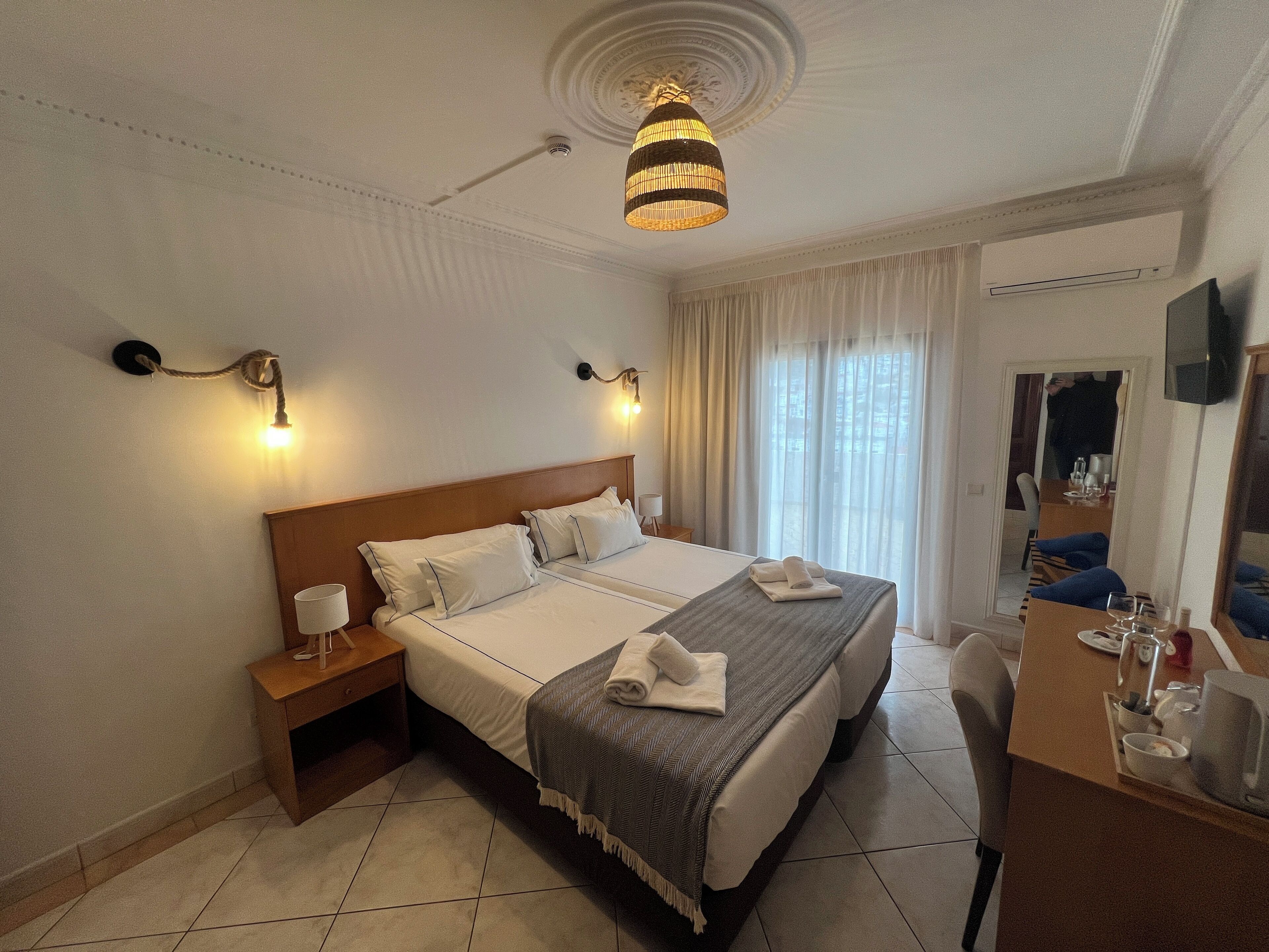 A hotel room with a large bed, bedside tables, a desk with a chair, and a television.