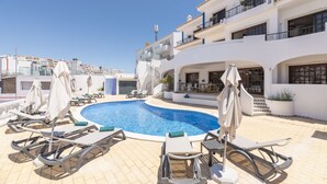A rooftop swimming pool with lounge chairs and umbrellas, surrounded by a white building with balconies. - ETHOS Bertolina Wellness Urban Living. (Albufeira)