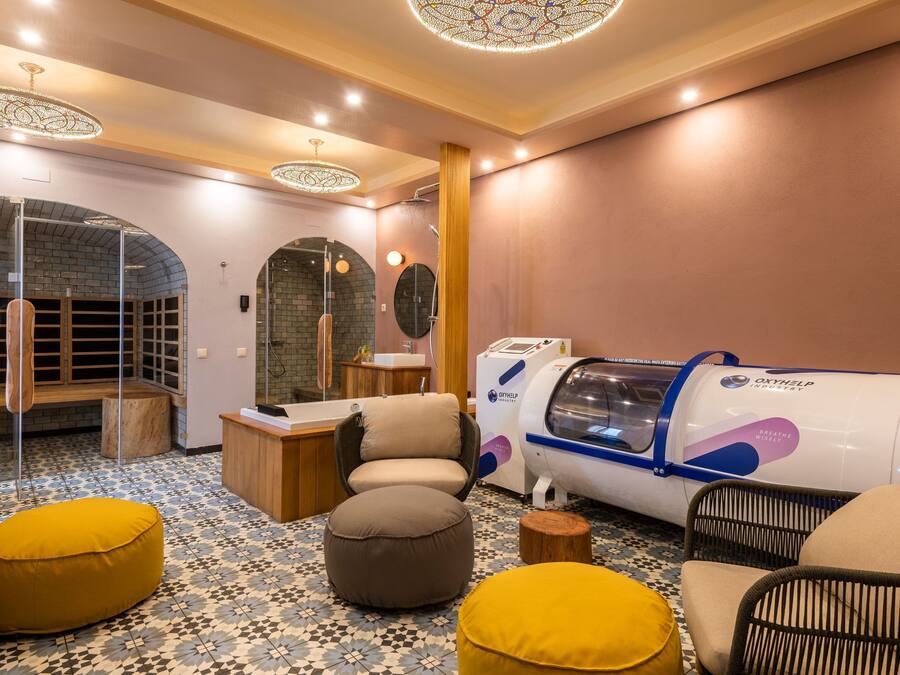 A modern spa room with a massage chair, a steam shower, and a body treatment machine.