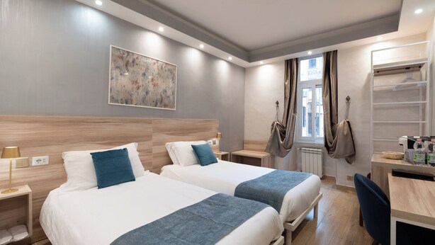 Habitación de hotel con dos camas, un escritorio, una silla y una ventana con cortinas.