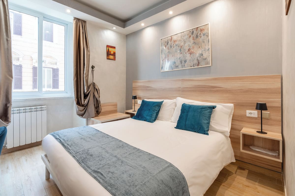 A modern hotel room with a large bed, a wooden headboard, and a view of the city through a window.