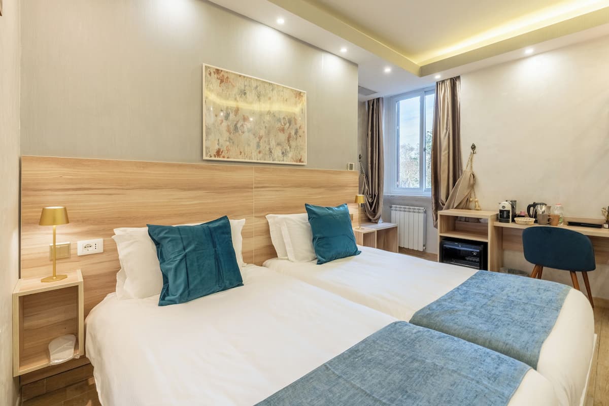 A hotel room with two beds, a desk, a chair, a lamp, and a window with curtains.