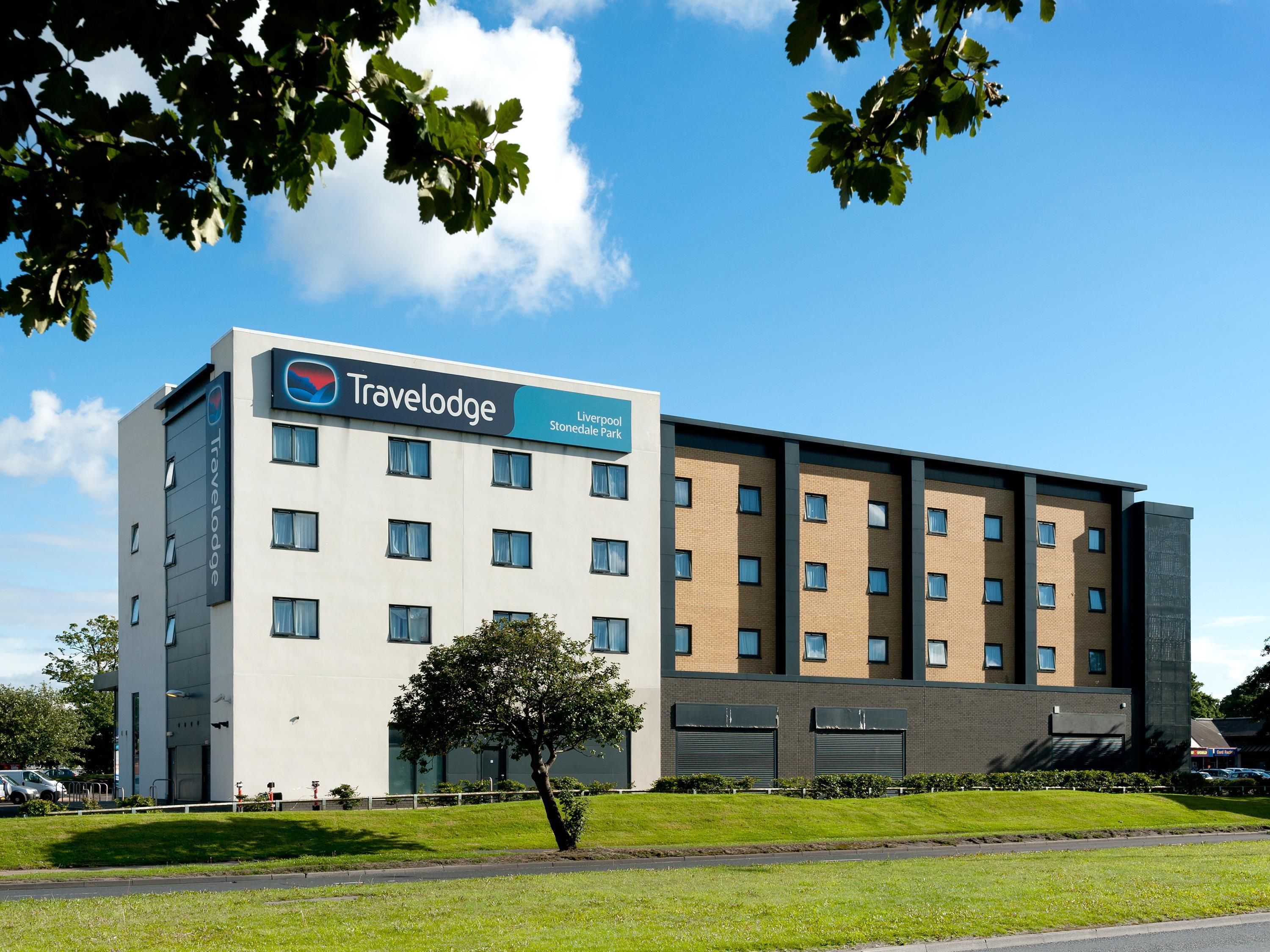 A Travelodge hotel with a modern design, featuring a flat facade, multiple windows, and a sign indicating its location at Liverpool Stonedale Park.