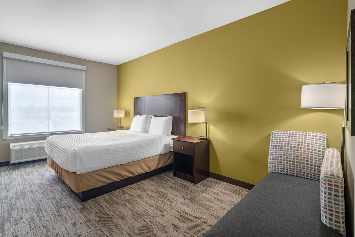 A hotel room with a bed, bedside tables, a chair, a window, and a lamp.